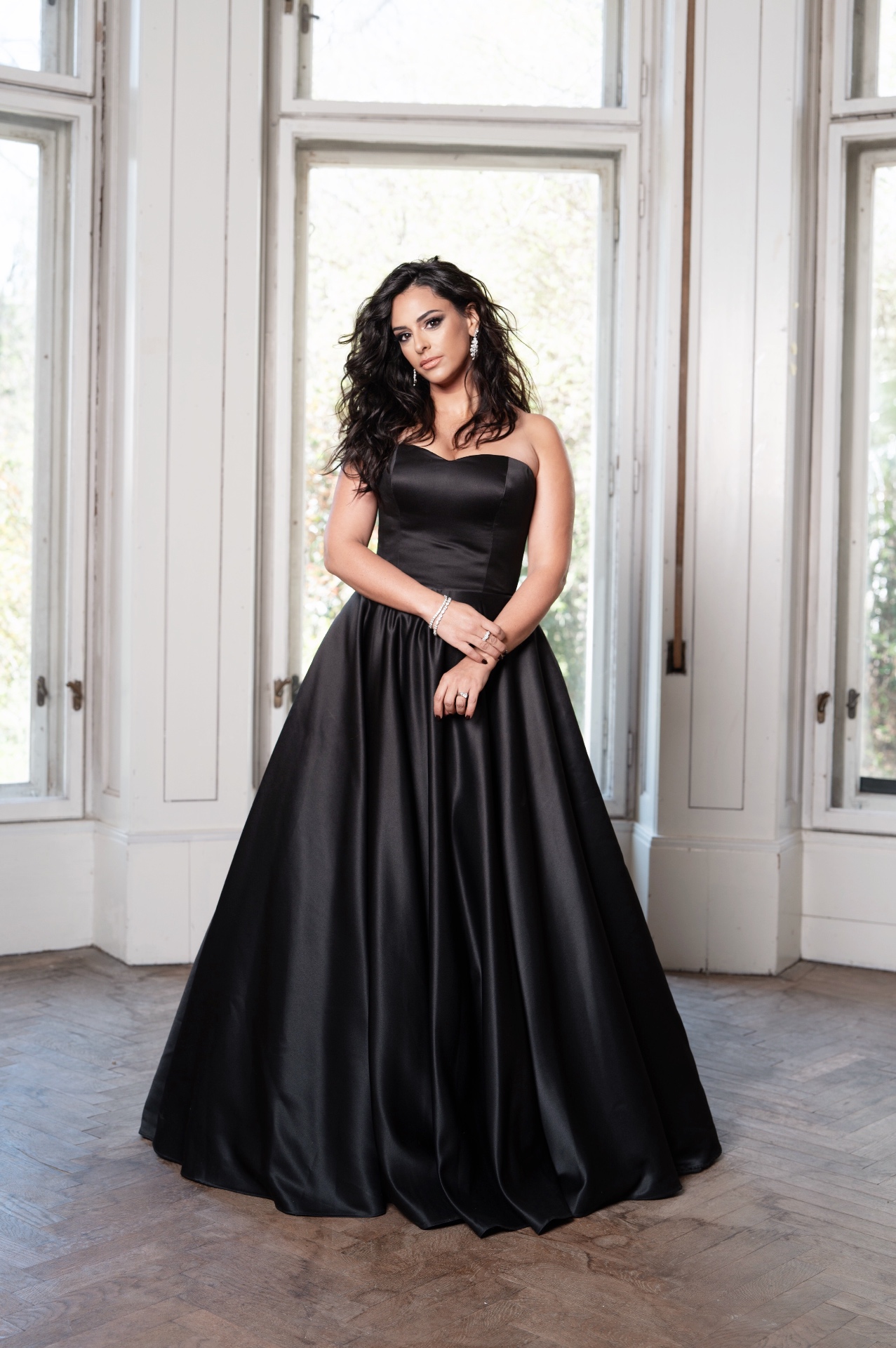 Hila Fahima in a black satin ball gown before tall white windows, by Manfred Baumann, 2025