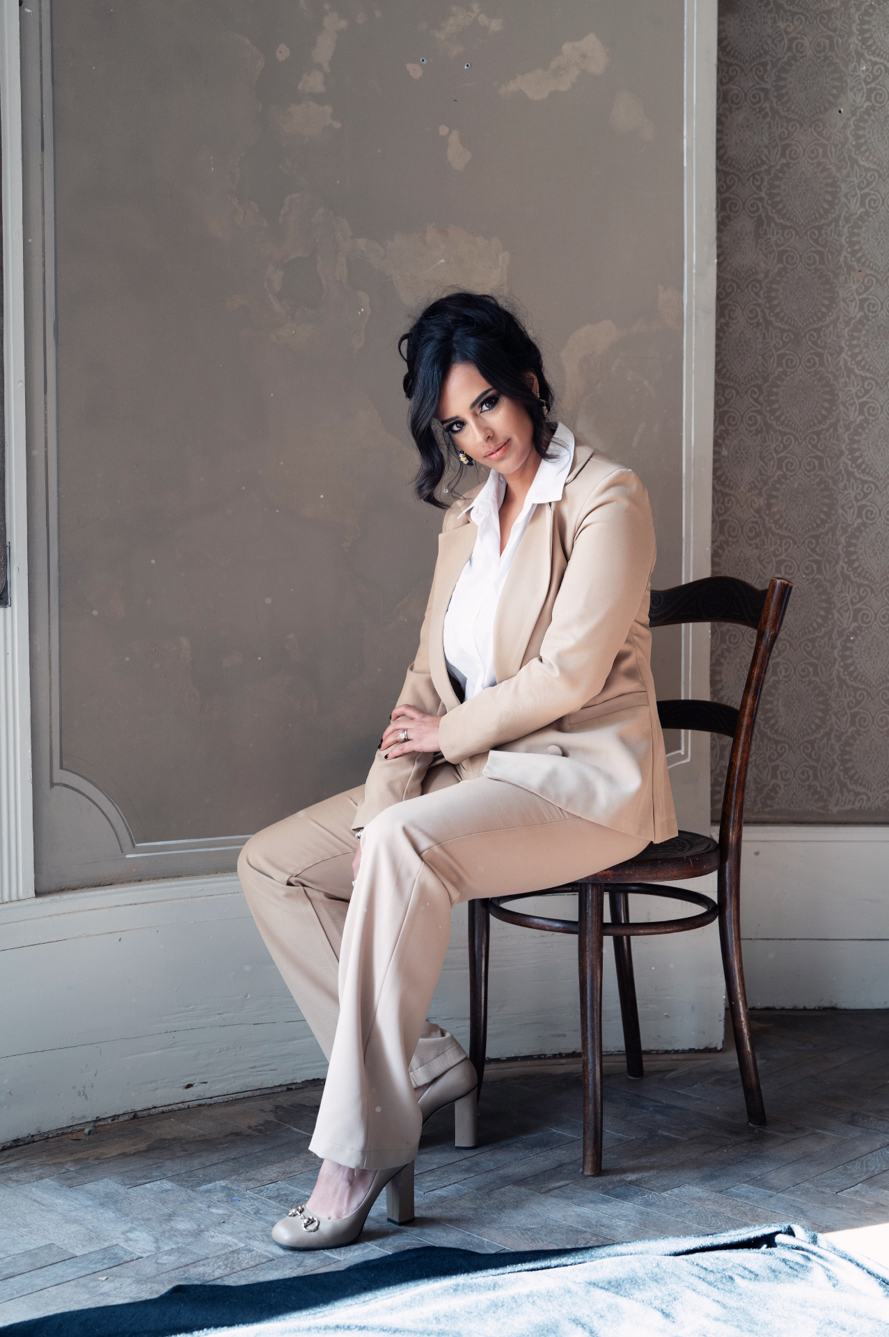 Hila Fahima seated on a bentwood chair in a beige suit, by Manfred Baumann, 2025