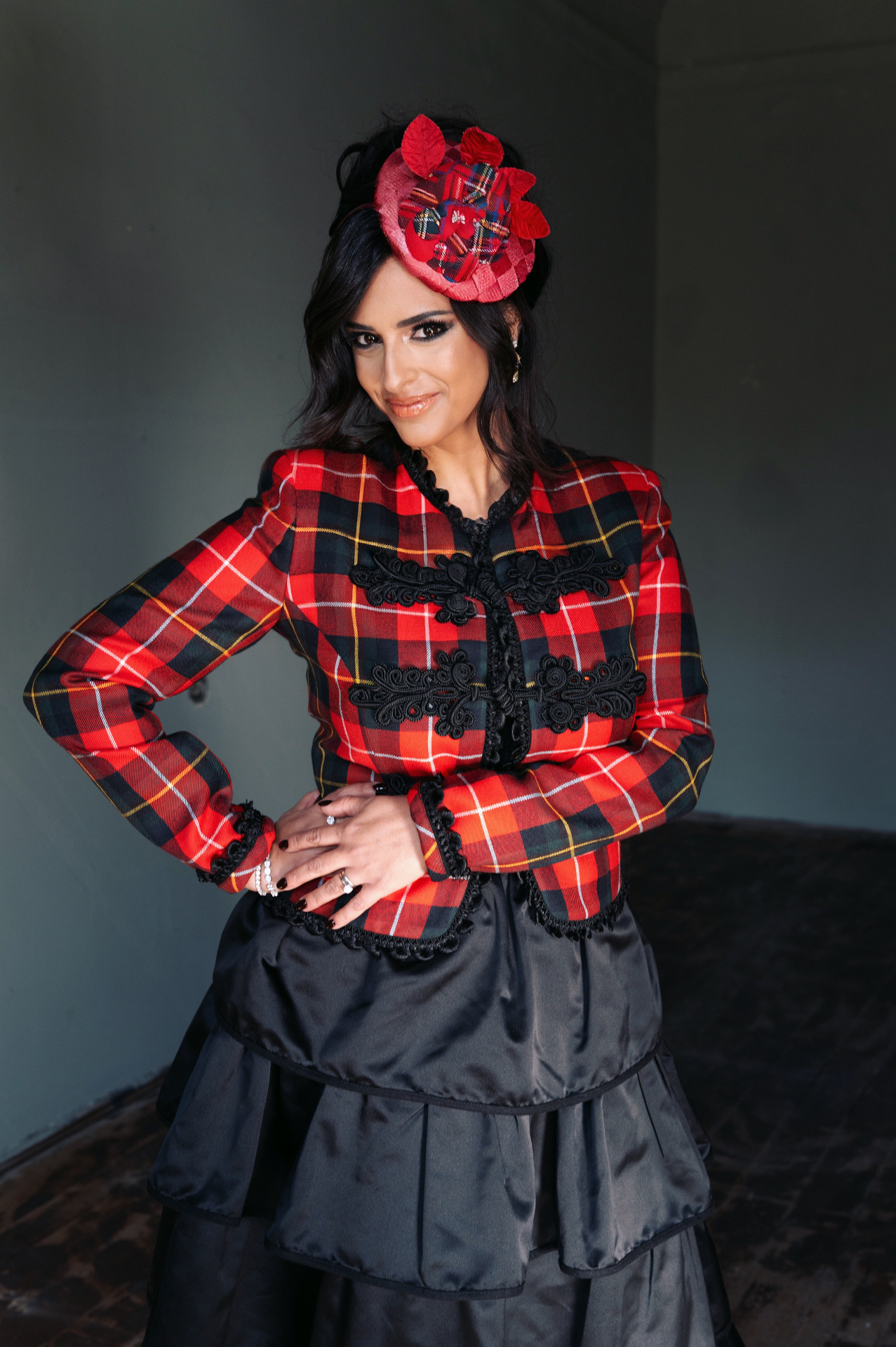 Hila Fahima in a red tartan jacket and black taffeta skirt with a matching hat, by Manfred Baumann, 2025