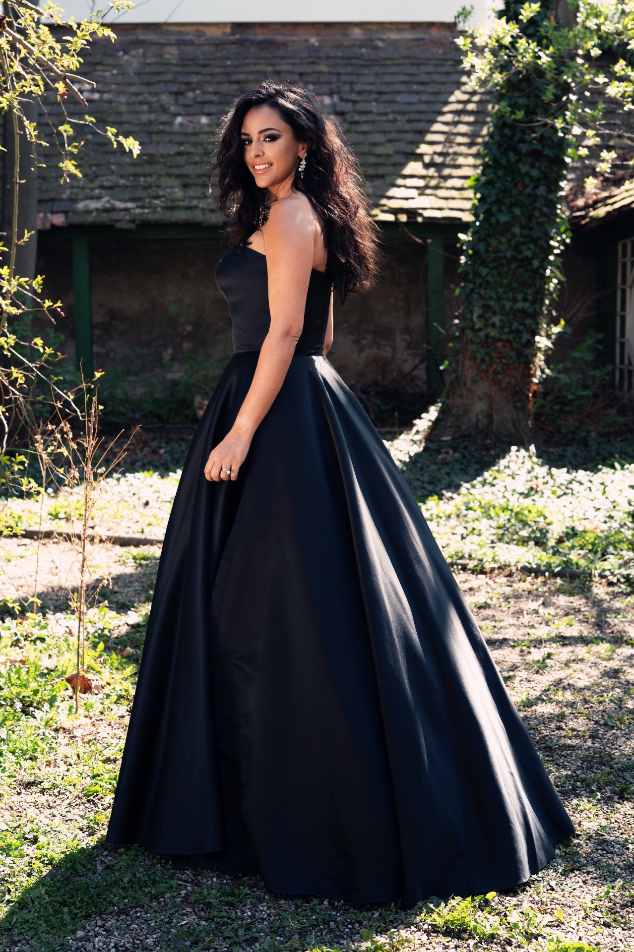 Hila Fahima in a black satin ball gown in a sunlit garden, by Manfred Baumann, 2025
