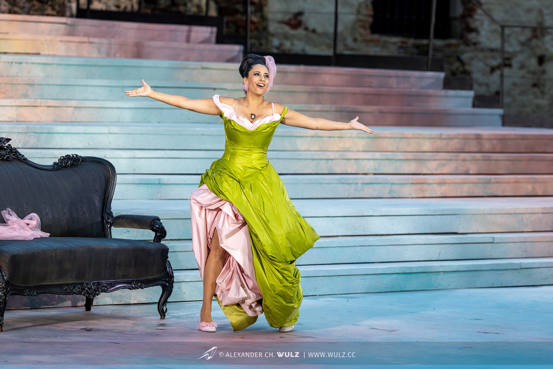 Hila Fahima as Violetta in La traviata, Oper Burg Gars 2025 — arms outstretched in a chartreuse gown with pink underskirt, photo by Alexander Wulz