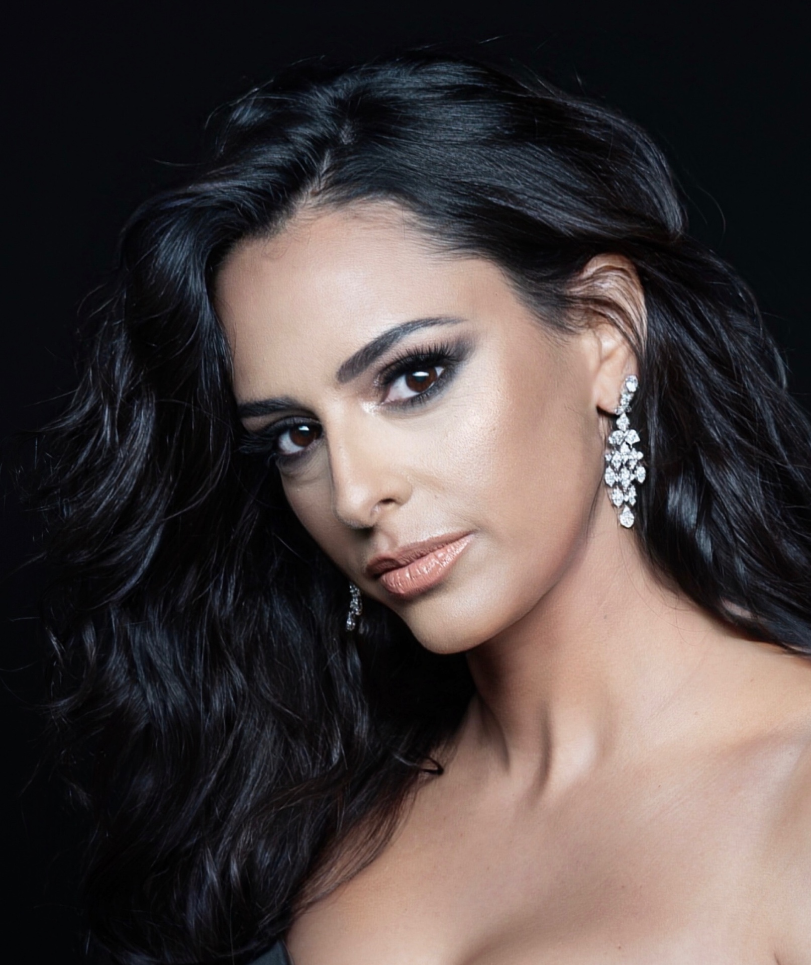 Close-up portrait of Hila Fahima with diamond chandelier earrings against a black backdrop, by Manfred Baumann, 2025